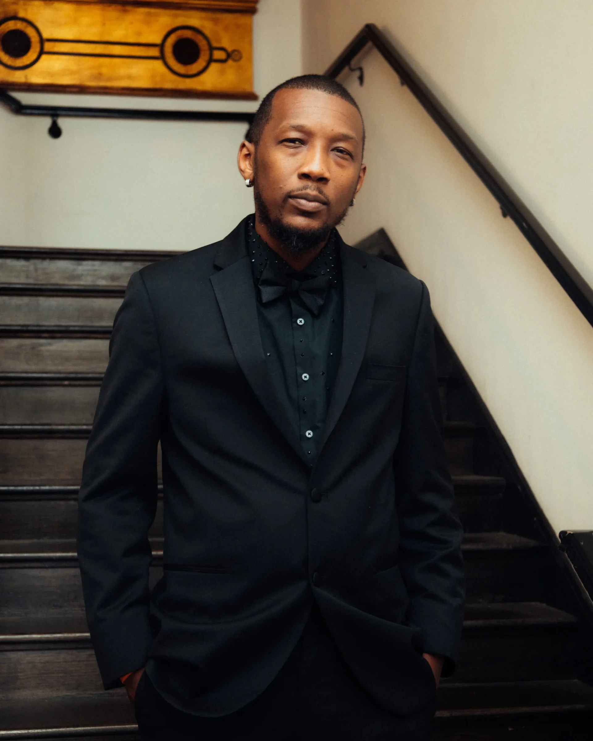 Photo of John Lacarbiere III in a black suit in front of a stairwell