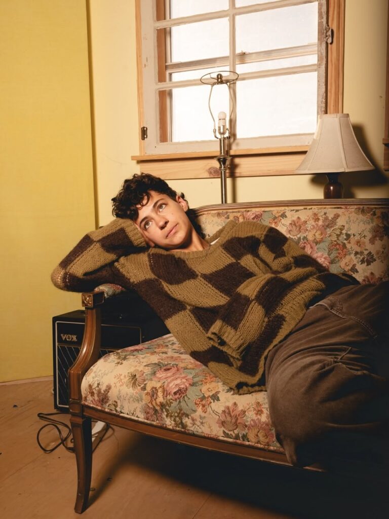 Man with dark hair and brown-and-tan sweater reclining on floral-patterned sofa.