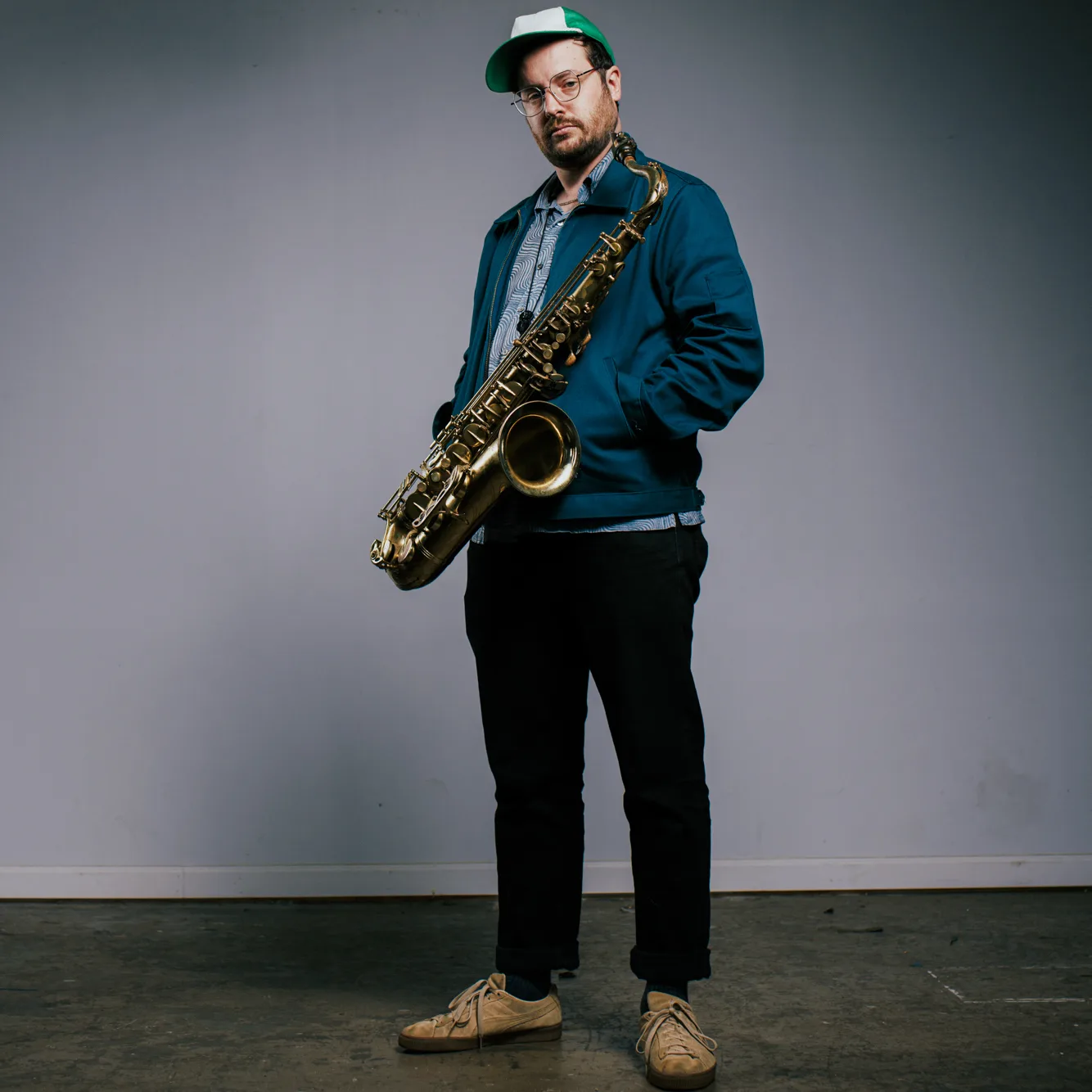 Photo of Byron Asher holding his saxophone in front of a grey wall.